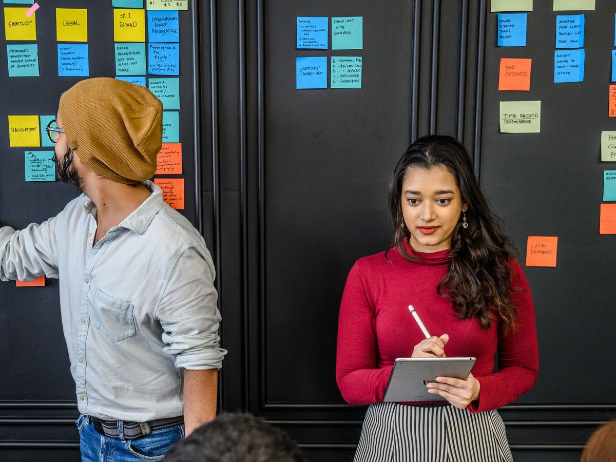 A team working in front of a wall of colorful sticky notes, one person taking notes on a tablet