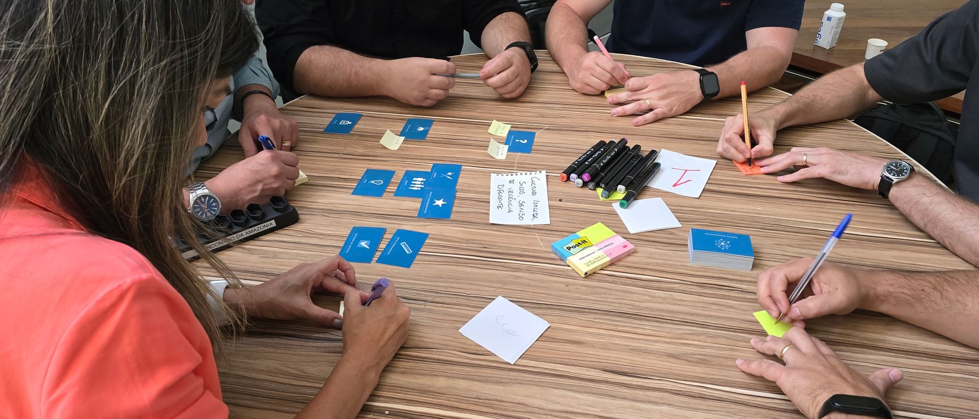 A group working around a wooden table covered in cards and sticky notes during a workshop